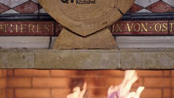 Eine hölzerne Plakette mit der eingravierten Aufschrift 'QIHOTELS' und 'Kitzbühel', an einem Kamin mit sichtbaren Flammen befestigt.