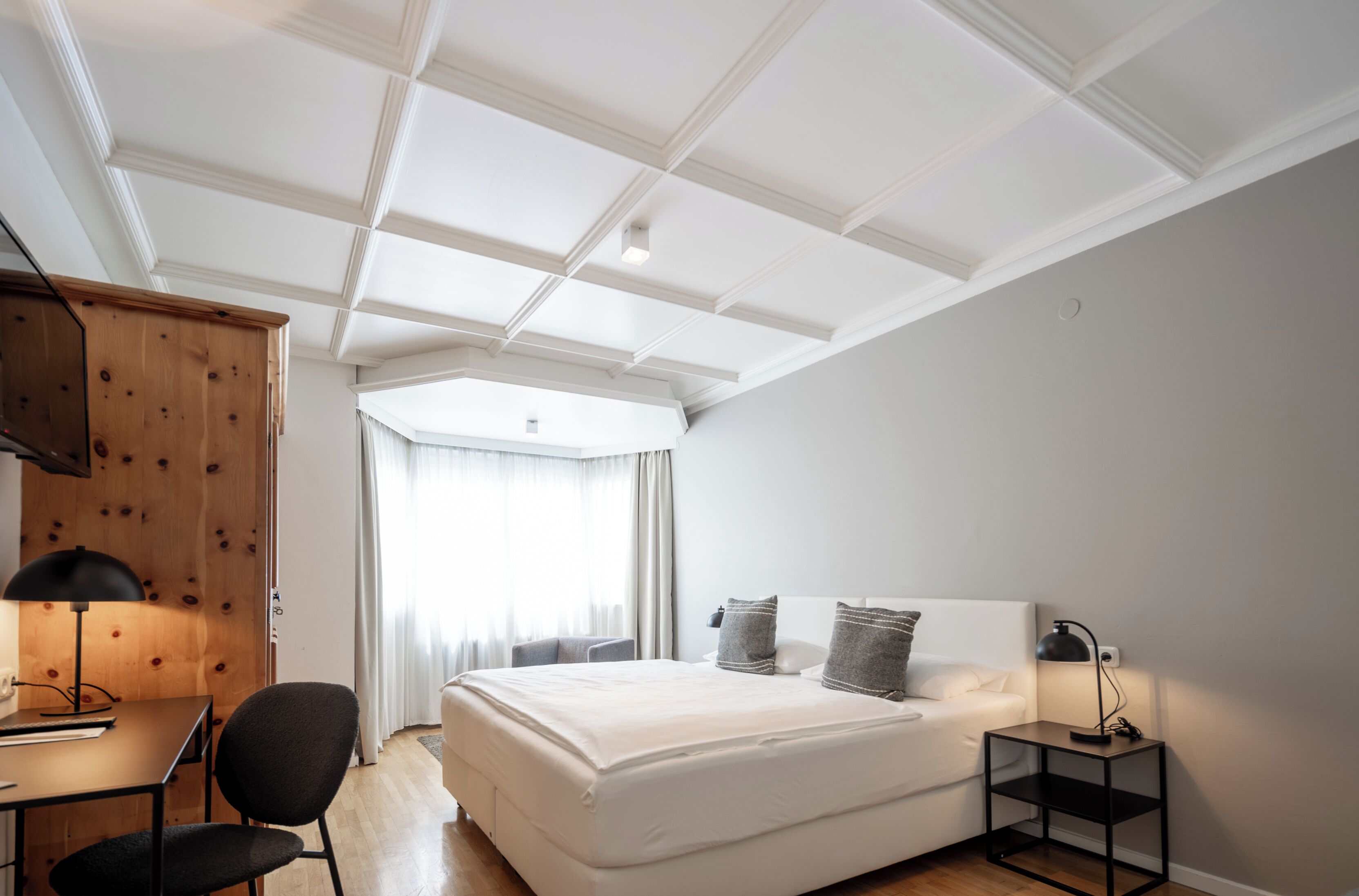 A modern bedroom with a large bed, a desk, a chair, and a wardrobe.