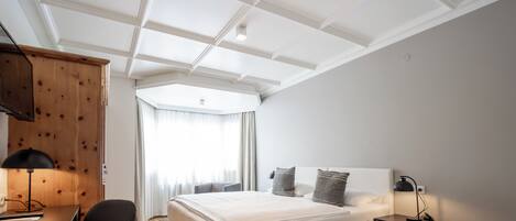 A modern bedroom with a large bed, a desk, a chair, and a wardrobe.