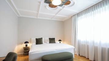A hotel room with a bed, two bedside tables, a chair, a ceiling fan, and a window with curtains.