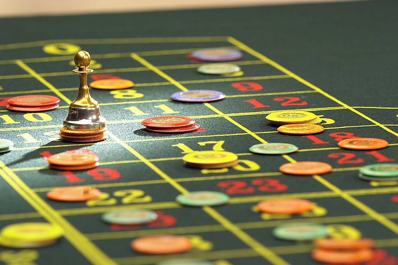 Een roulette tafel met een gouden dealerknop, kleurrijke fiches en nummers voor inzetten.