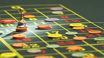 Een roulette tafel met een gouden dealerknop, kleurrijke fiches en nummers voor inzetten.