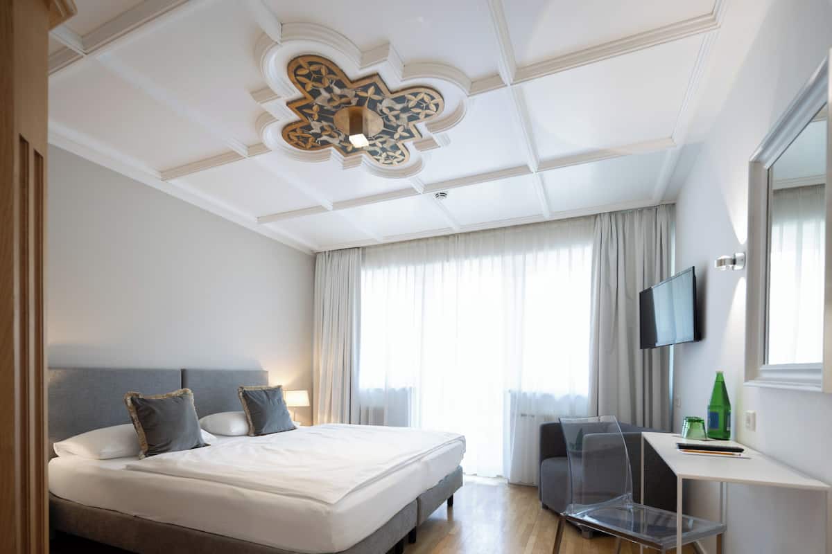 A hotel room with a large bed, a desk, a chair, a television, and a window with curtains.