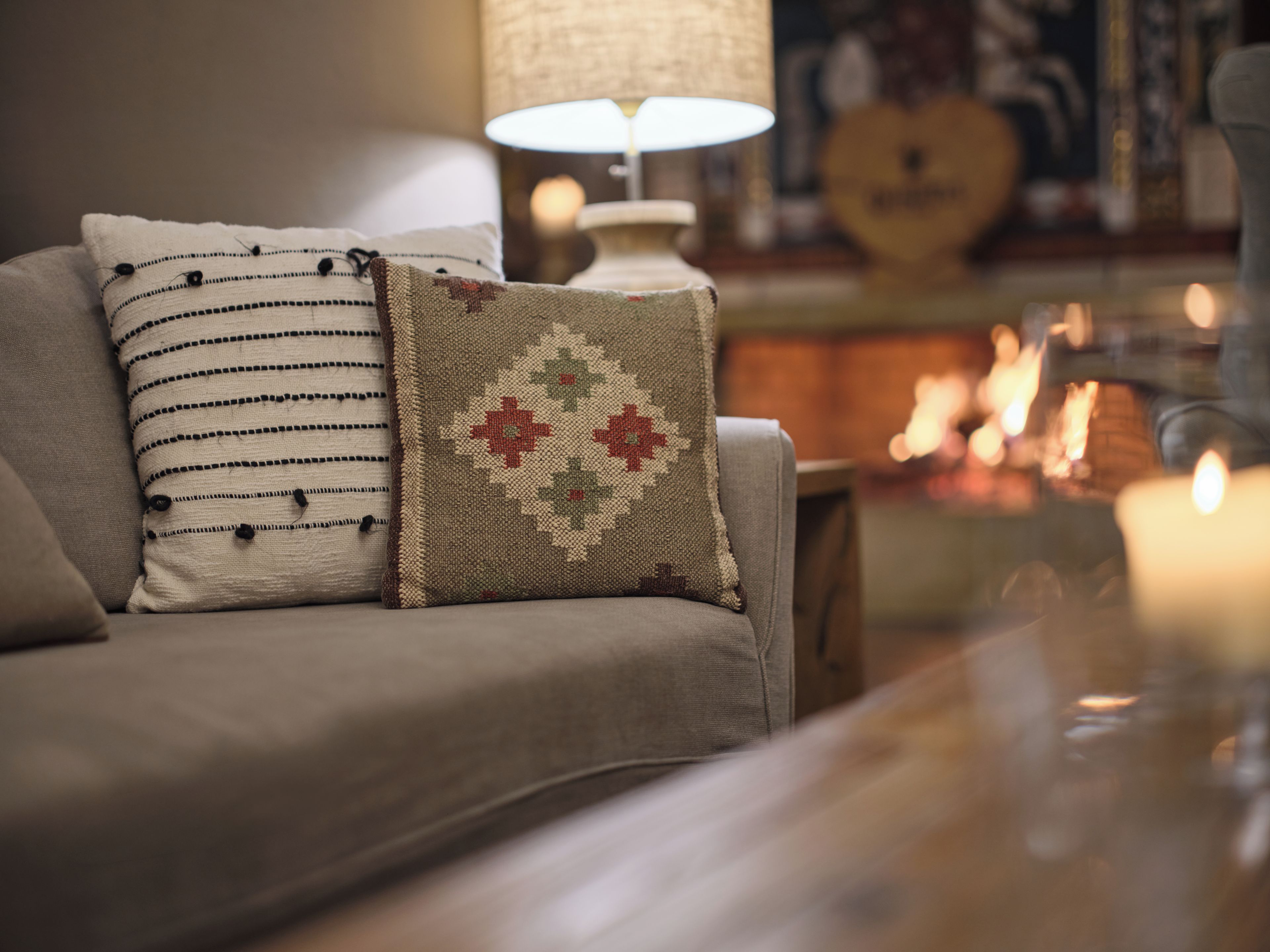 Un sofá con dos almohadones decorativos, una lámpara y un fondo desenfocado con una guitarra y velas.