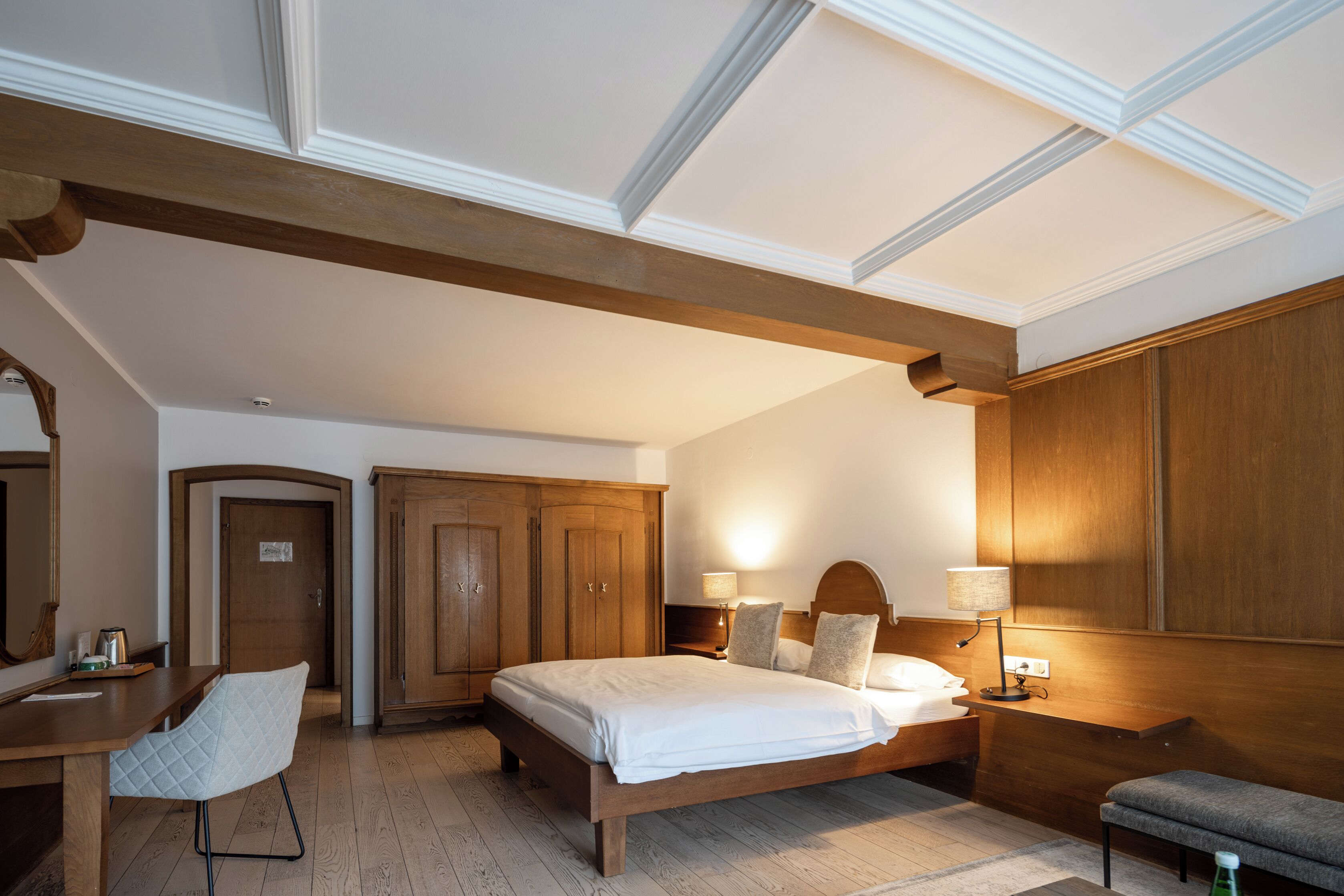 A hotel room with a wooden bed, a desk, a chair, and a wardrobe.