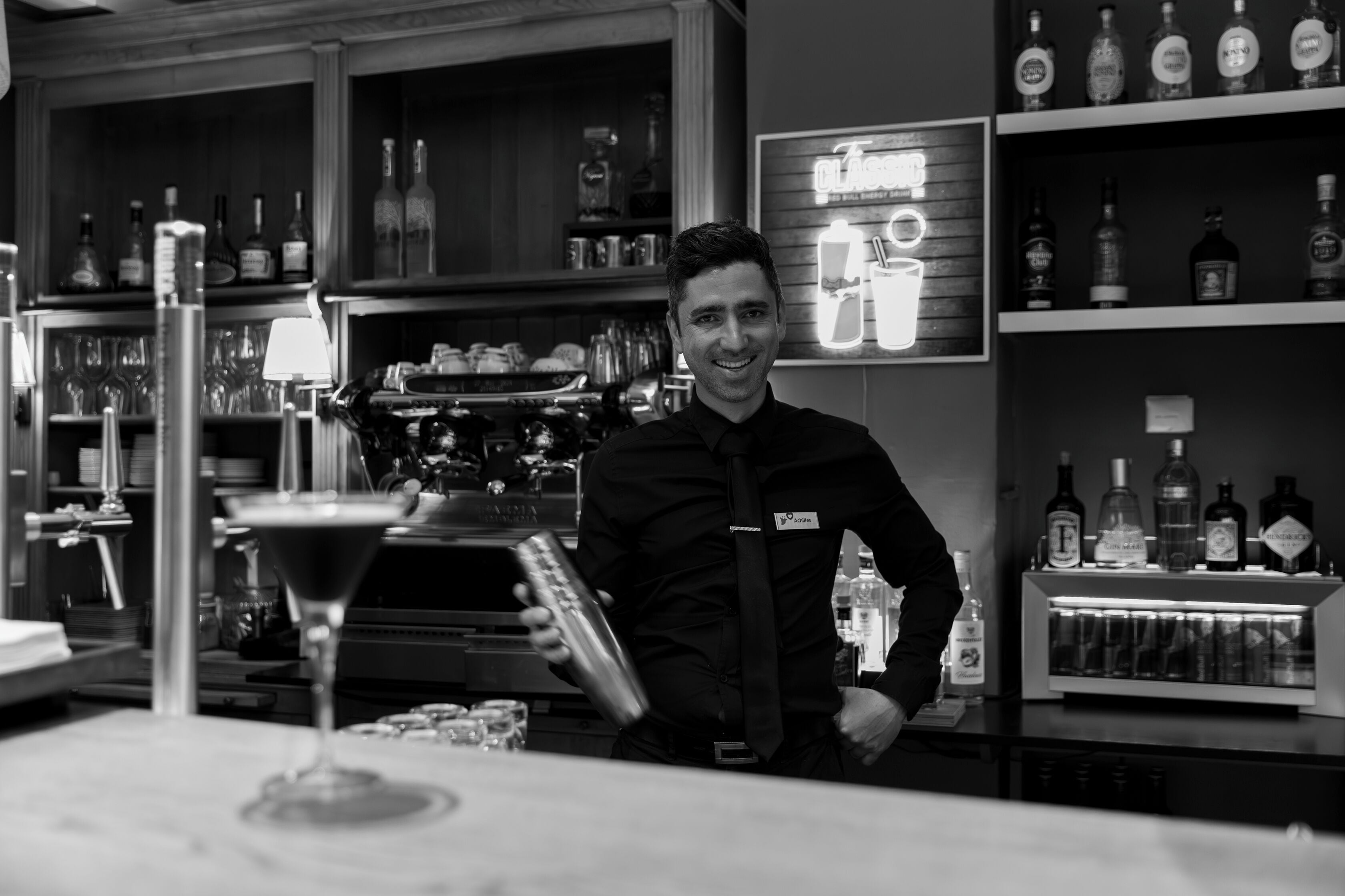 A bar area with shelves of liquor bottles, a bar counter, and a bartender preparing a drink.