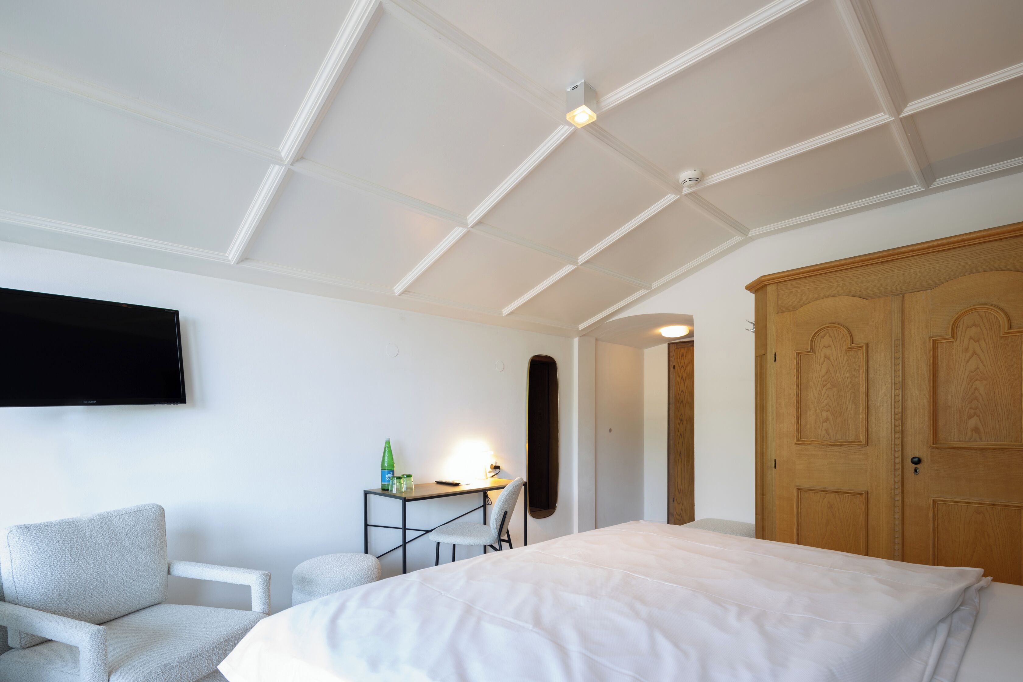 A bedroom with a bed, a desk, a chair, a wardrobe, and a television on the wall.