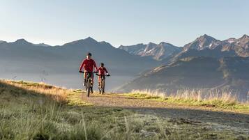 Deux personnes à vélo sur un chemin de terre, avec des montagnes en arrière-plan.