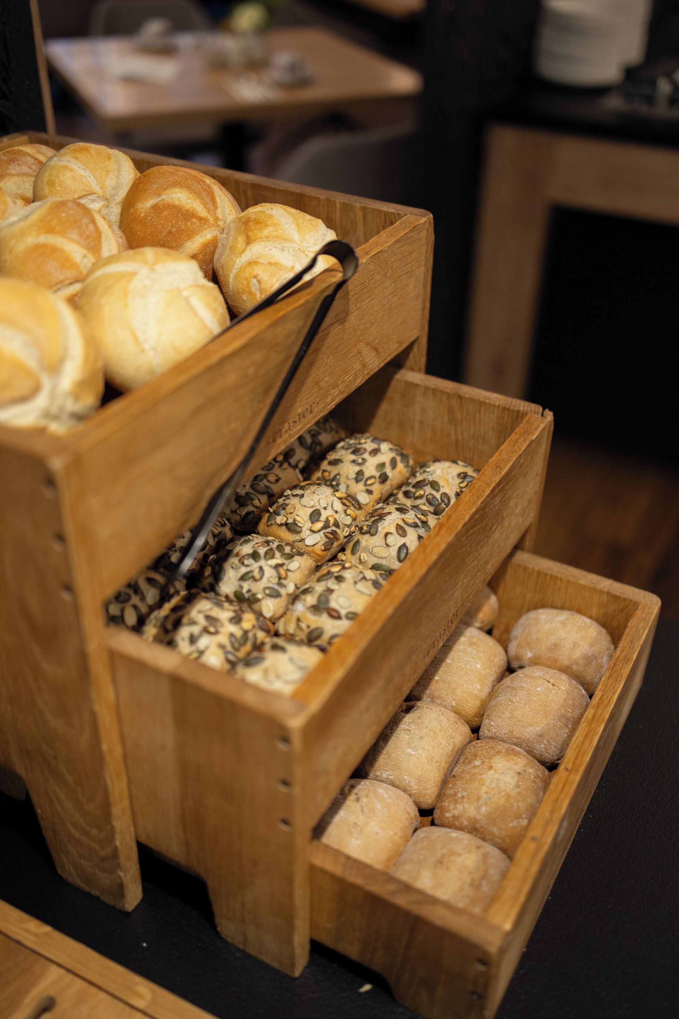 Una vitrina de madera con distintos tipos de pan, incluyendo bollos con semillas y hogazas redondas.