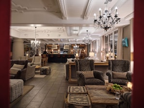 A spacious lounge area with a bar, comfortable seating, and a chandelier. - Q Hotel Maria Theresia (Kitzbuhel)
