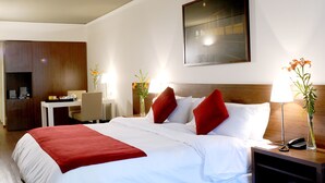 A hotel room with a large bed, a desk, a chair, and a nightstand with a lamp and phone. - Dazzler by Wyndham Buenos Aires Maipu (Buenos Aires)