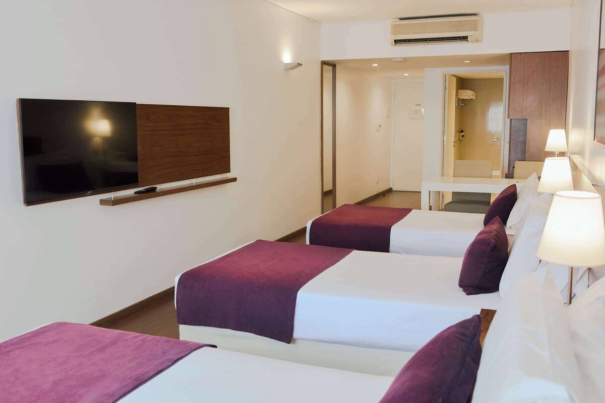 Ein Hotelzimmer mit zwei Betten, einem Fernseher, einem Schreibtisch und einem durch eine offene Tür einsehbaren Badezimmer.
