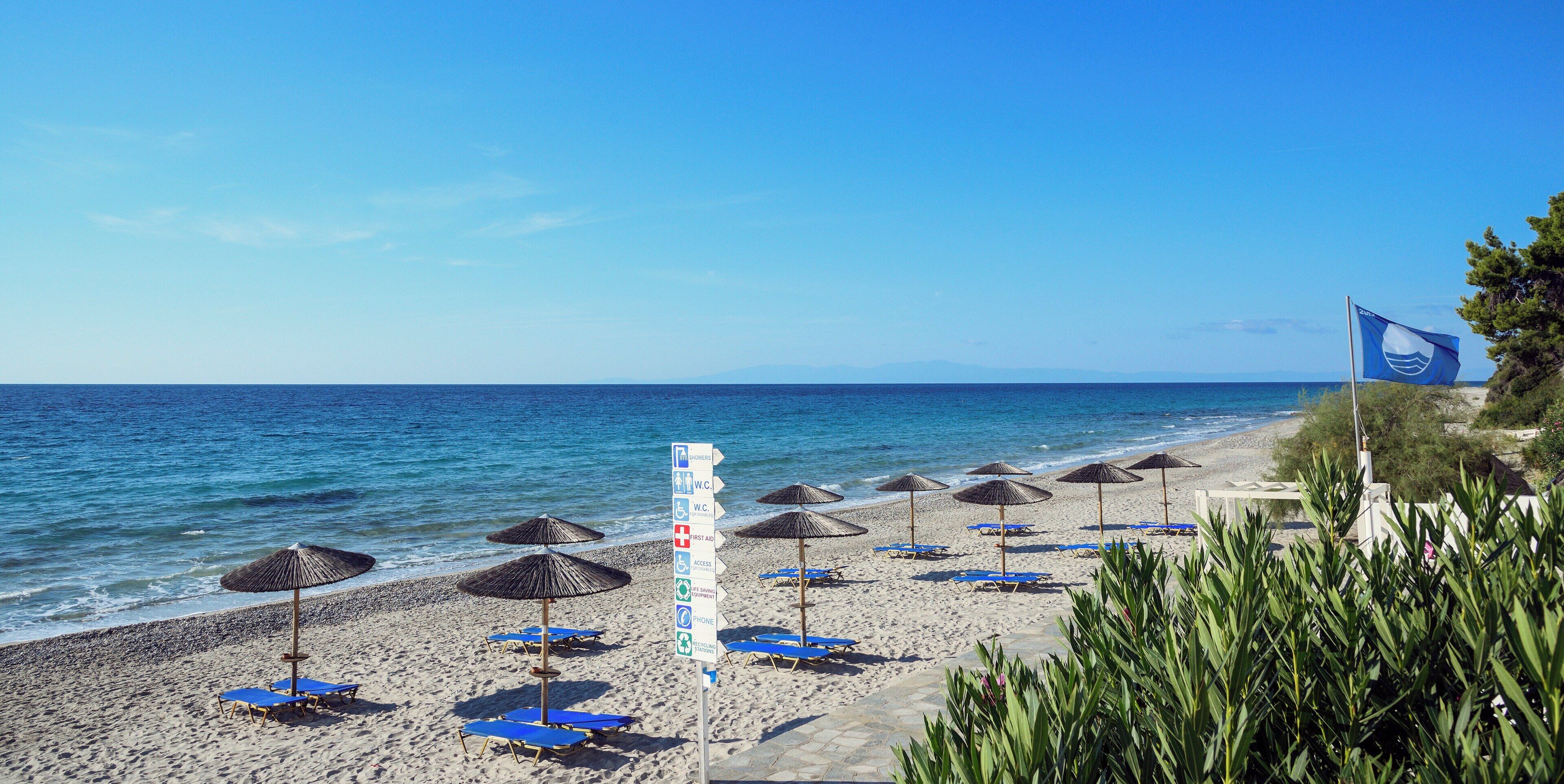 A beach with umbrellas and lounge chairs, a signpost with amenities, and a flag.
