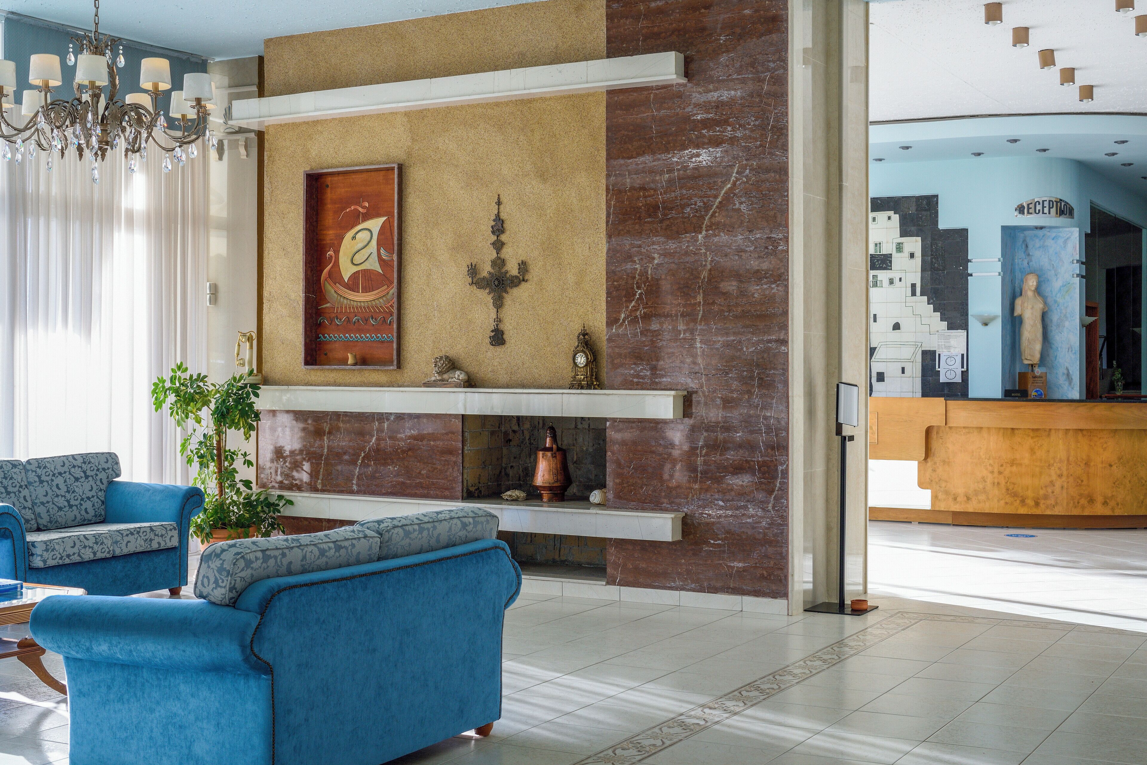 A lobby with a reception desk, blue sofas, a chandelier, and a decorative wall with a framed artwork and a candelabra.