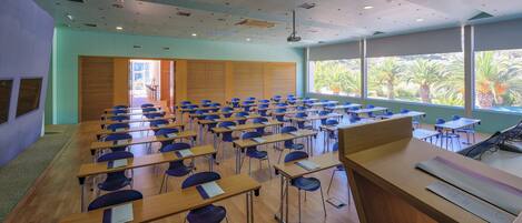 A classroom with rows of desks and chairs, large windows with a view of palm trees, and a door leading outside.