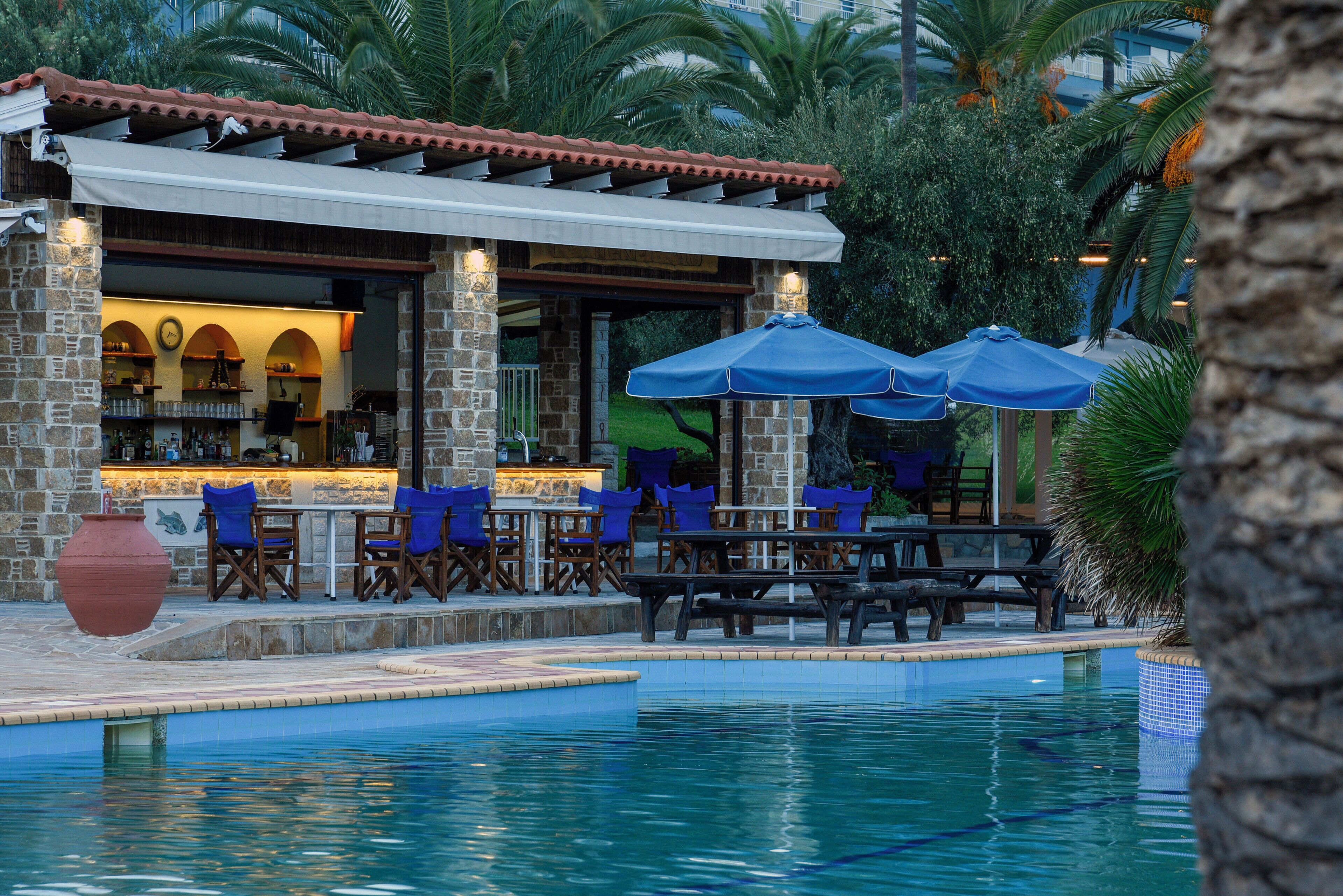 An outdoor pool area with stone and wood structures, blue chairs, and umbrellas.