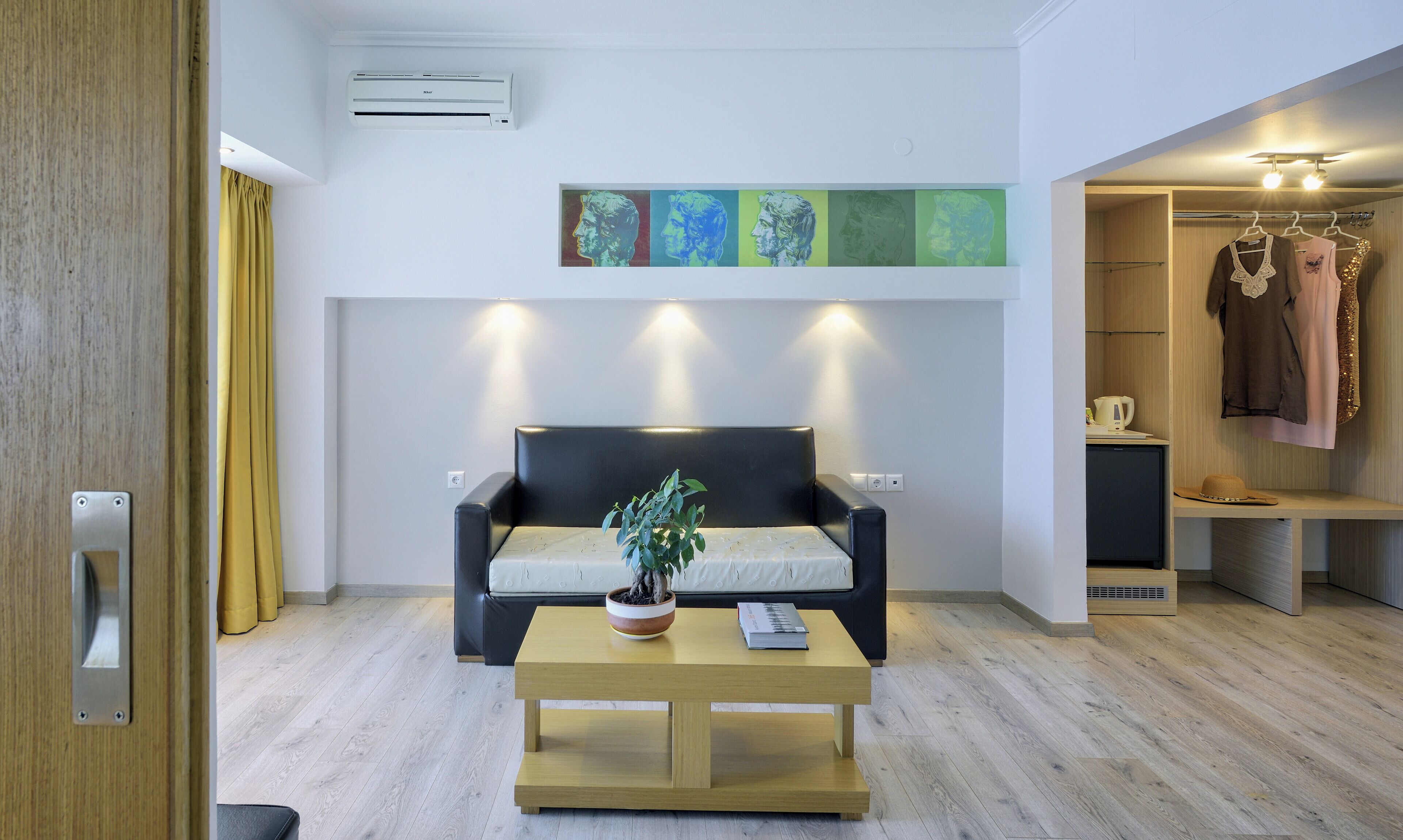 Una sala de estar moderna con un sofá negro, una mesa de centro de madera con una planta en maceta y un aire acondicionado instalado en la pared.