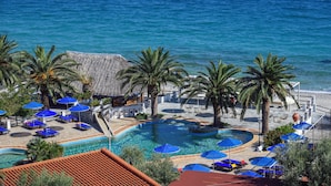 Un área de piscina en un resort con múltiples sillas de descanso y sombrillas, rodeada de palmeras y vista al océano.