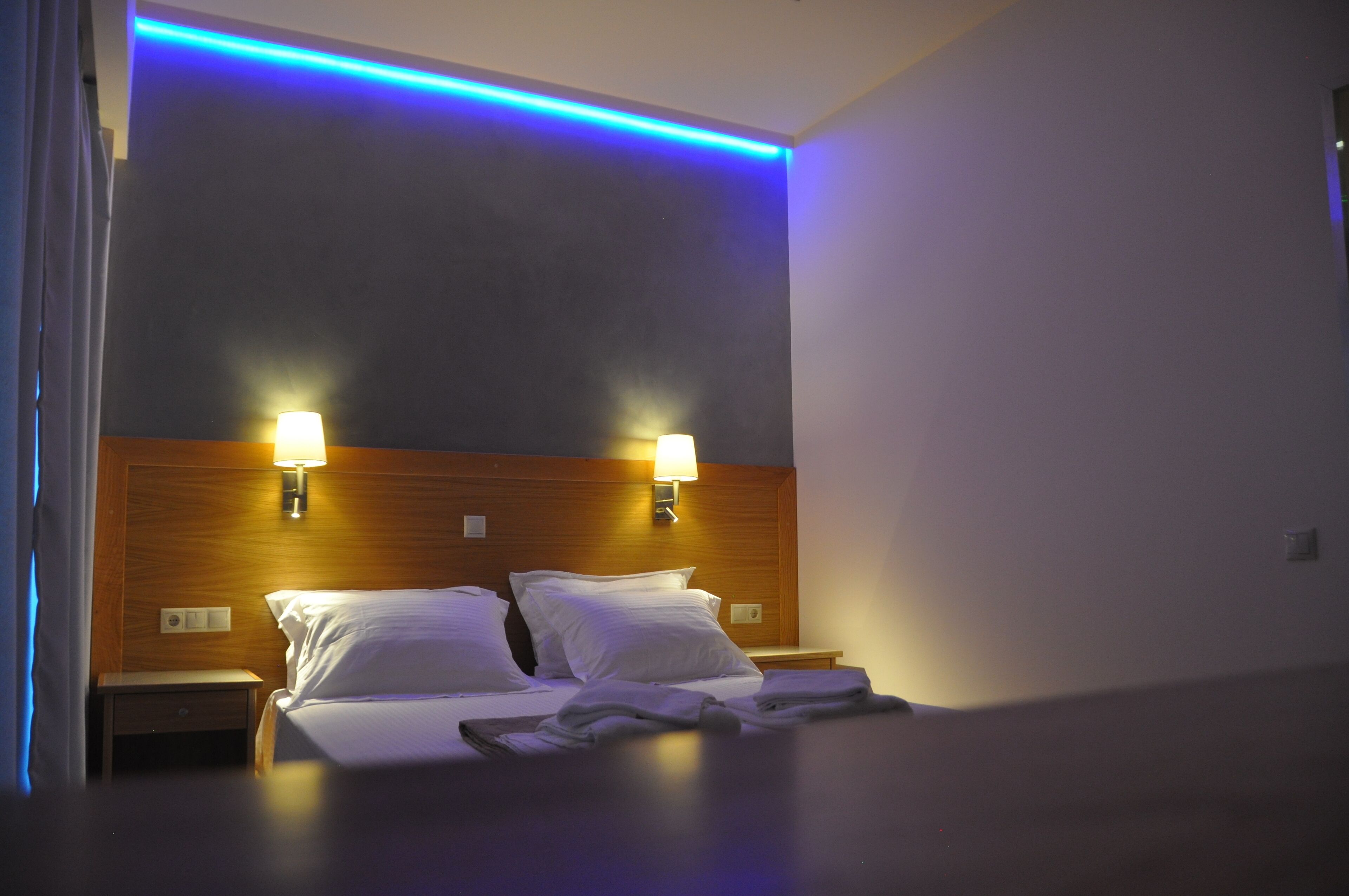Una habitación de hotel con cabecera de madera, dos lámparas de noche, una cama con ropa de cama blanca y una mesita de noche.