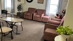 Habitación de hotel con zona de estar, una mesa de comedor, un reloj y un ventilador de techo.