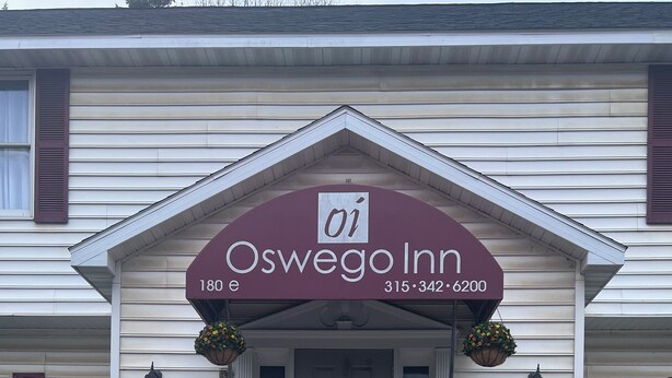 Un edificio de dos pisos con un porche delantero, un letrero que dice 'Oswego Inn' y una puerta con el rótulo '180E'.