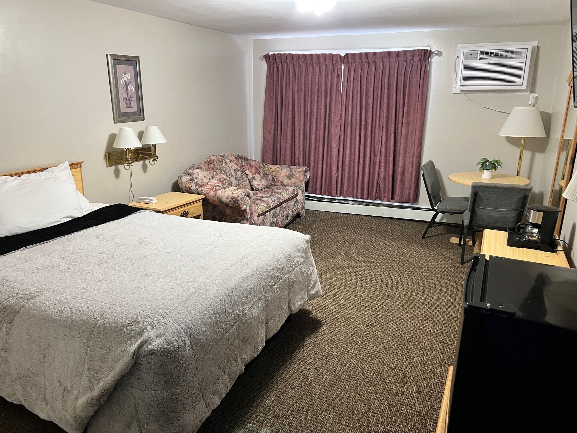 Habitación de hotel con una cama grande, un sofá, un escritorio con una silla, una mesita, una lámpara, aire acondicionado y un cuadro en la pared.