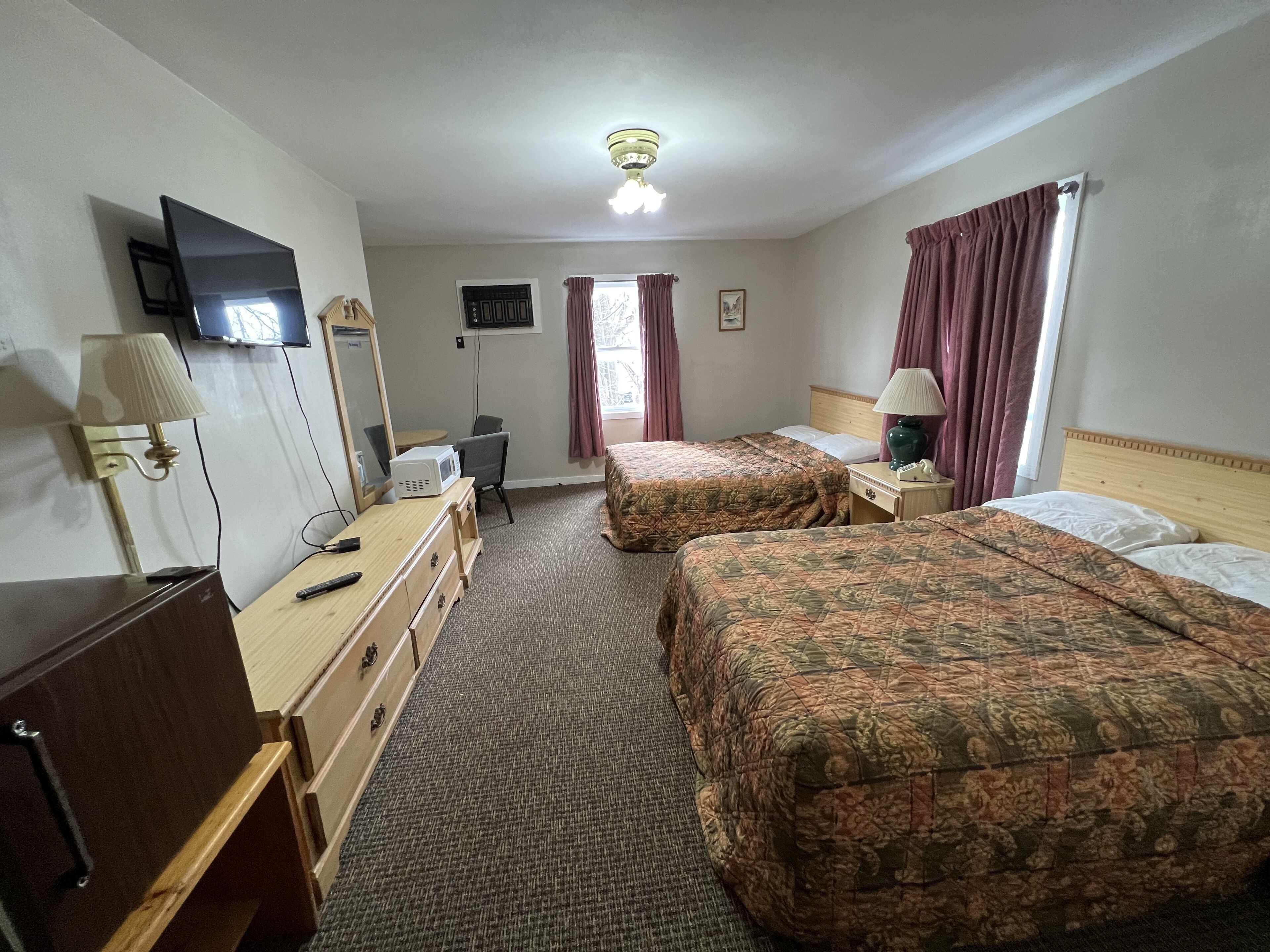 Une chambre d’hôtel avec deux lits, un bureau, une chaise, une télévision et un ventilateur de plafond.