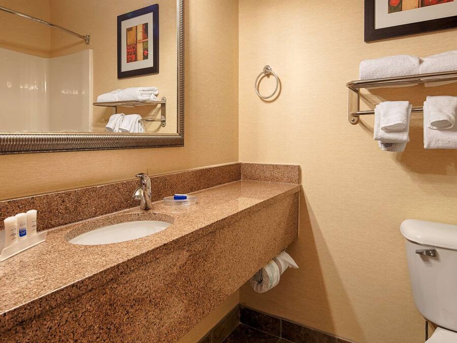 A bathroom with a granite countertop, a sink, a mirror, a towel rack, and a toilet.