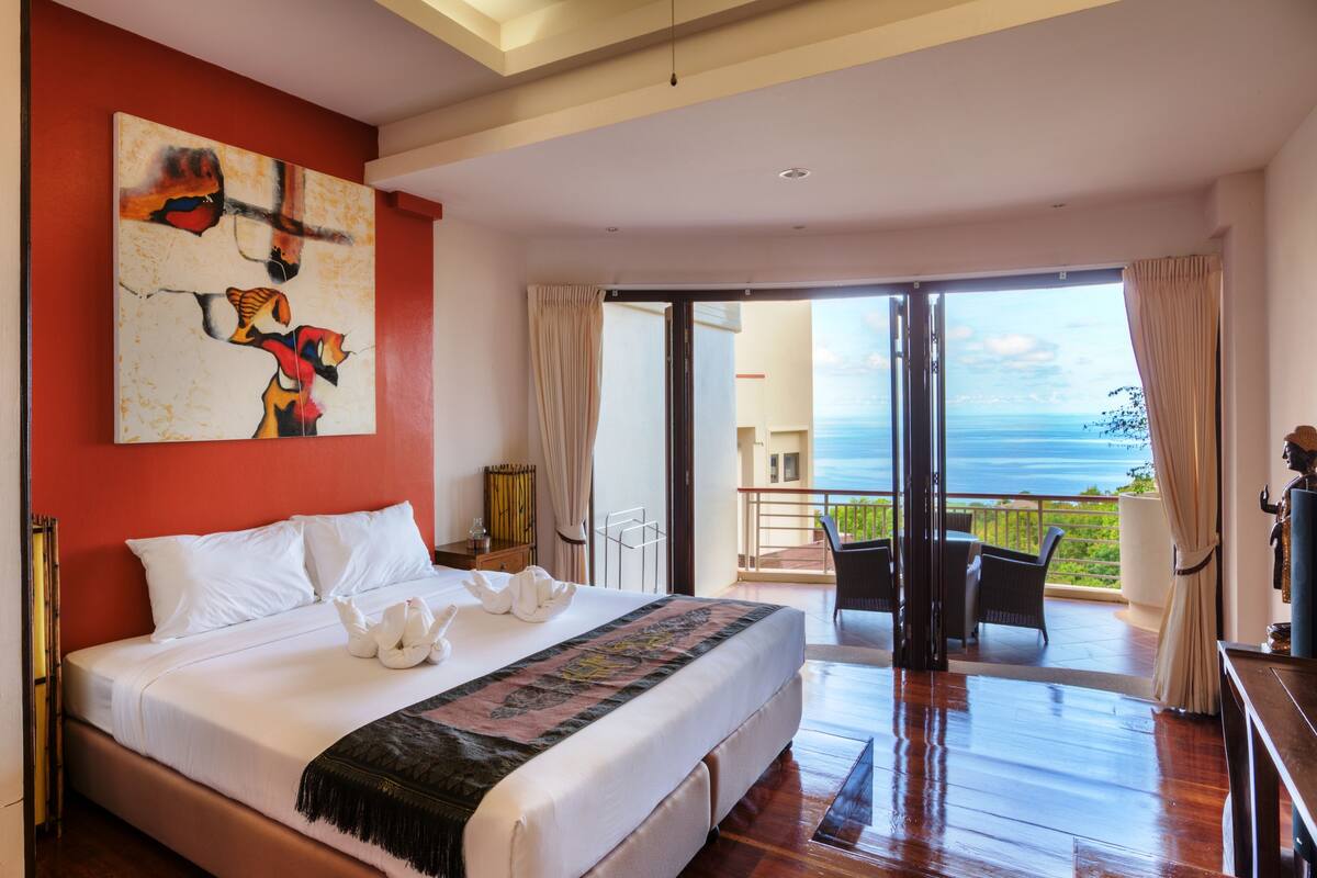 A spacious bedroom with a large bed, a view of the ocean, and a balcony with outdoor furniture.