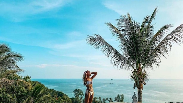 A woman in a bikini standing by an infinity pool with a view of the ocean.