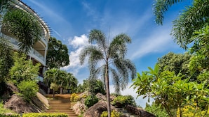 A staircase leading up to a building with a circular balcony, surrounded by lush greenery and large rocks.