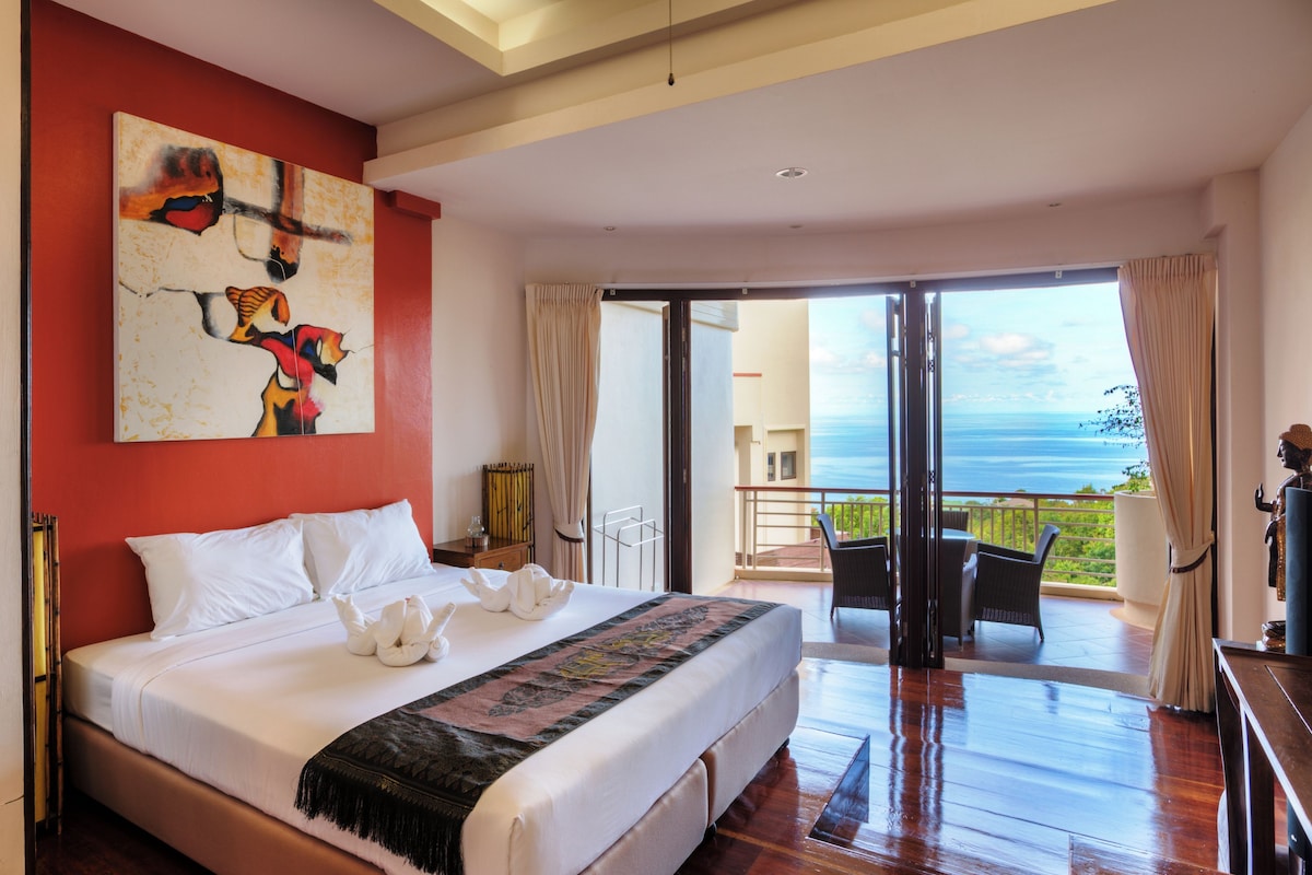 Un dormitorio amplio con una cama grande, vistas al océano y un balcón con mobiliario exterior.