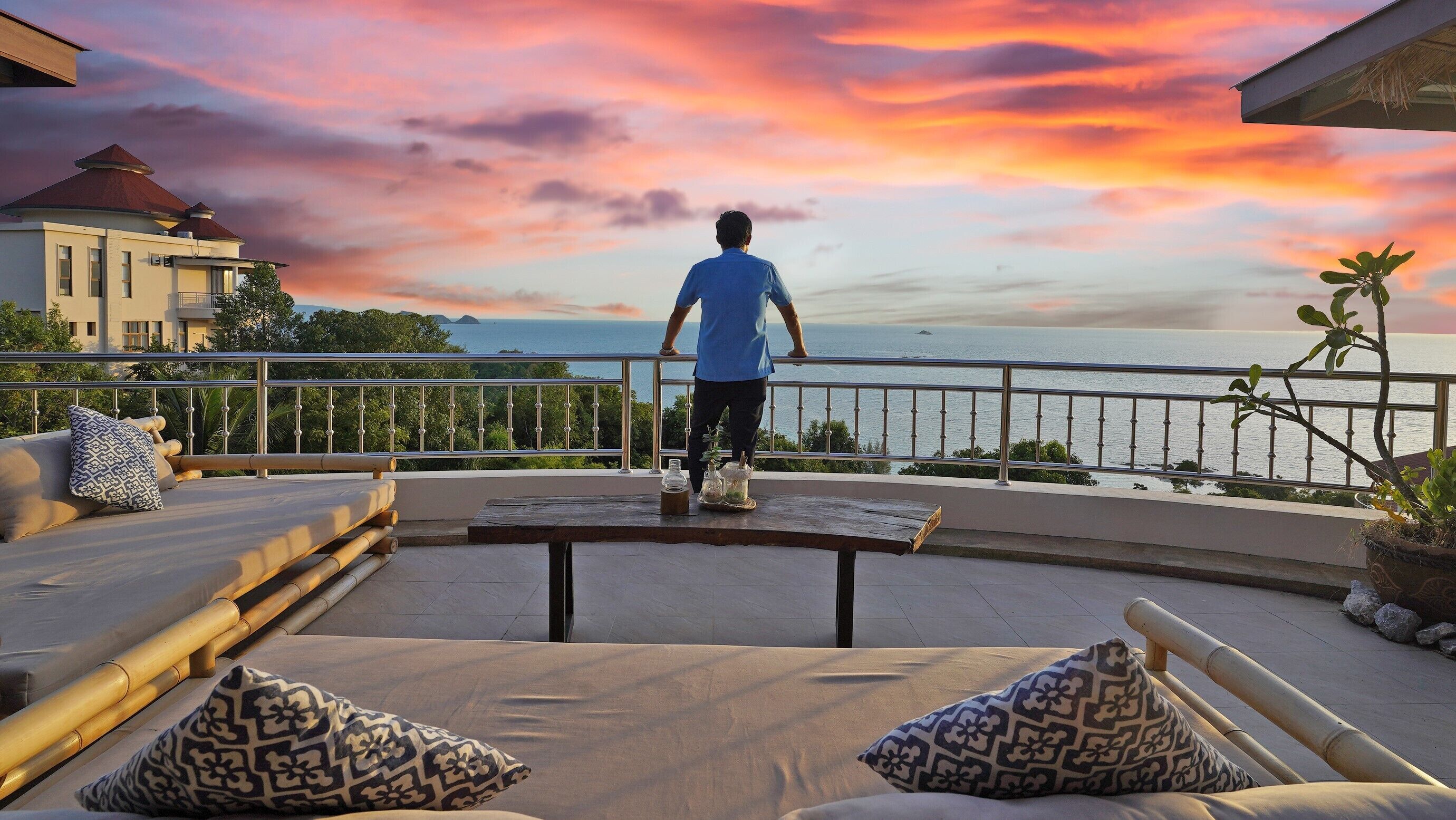 A man standing on a balcony overlooking a sunset with a view of the sea.