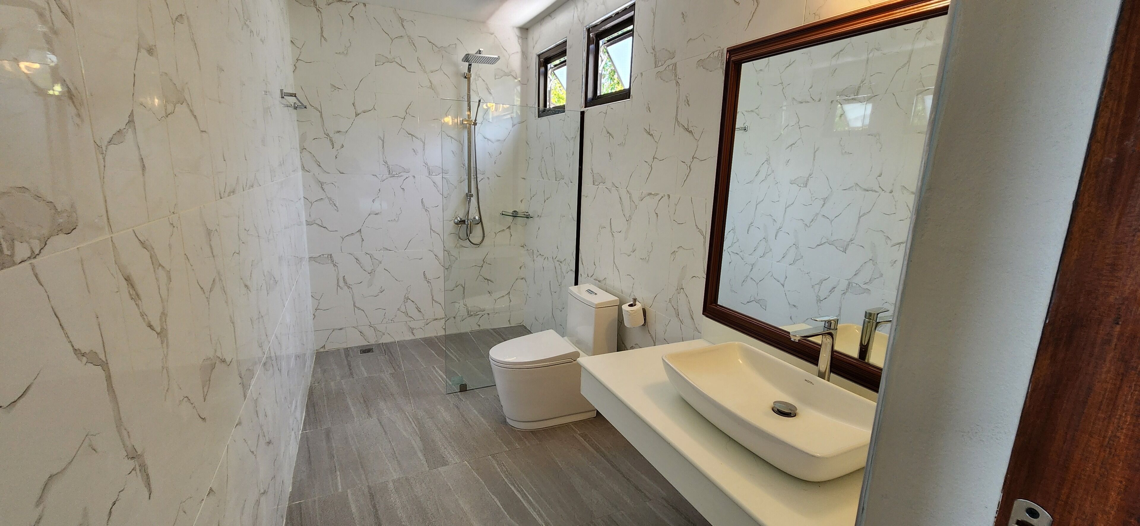 A bathroom with a marble wall, a shower, a toilet, and a sink with a mirror.