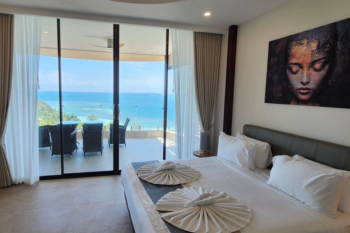 A hotel room with a large bed, a view of the ocean, and a painting on the wall.