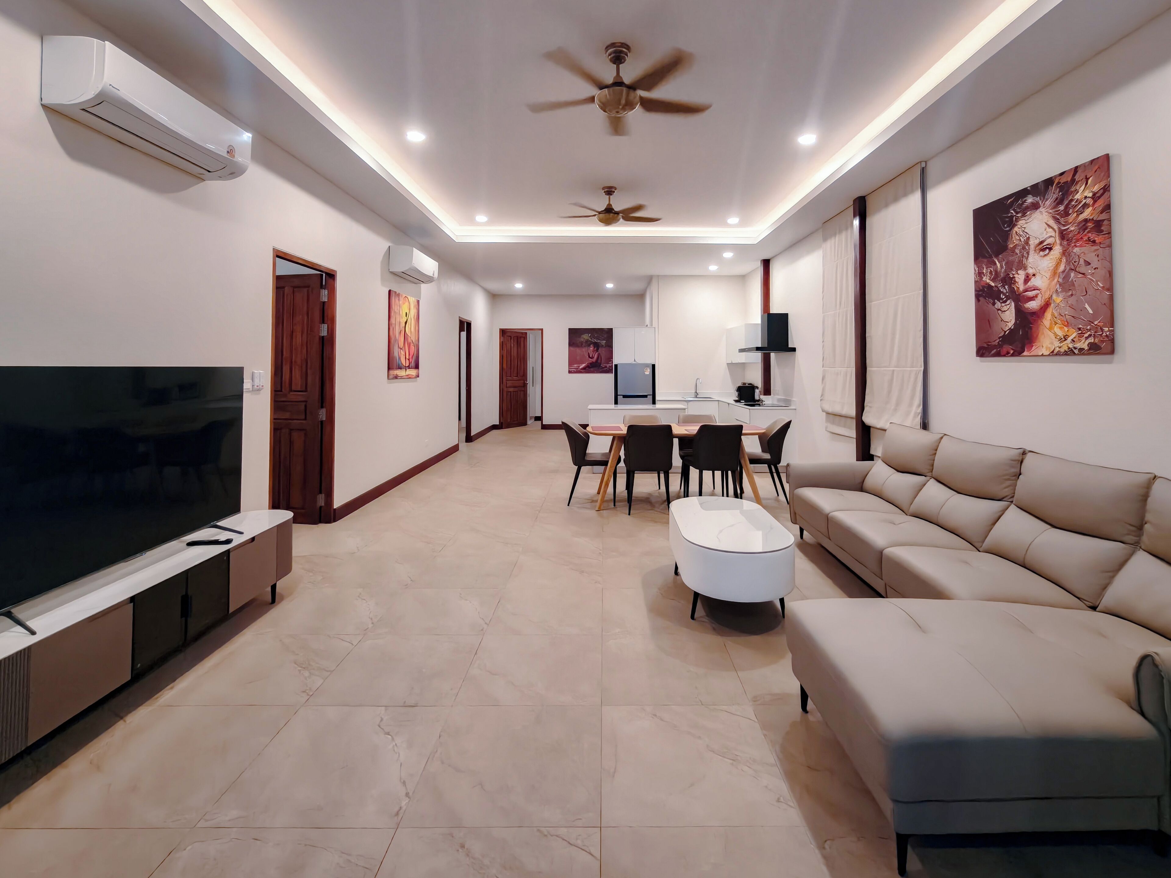 A modern living room with a flat-screen TV, a sofa, a dining area with chairs, and a ceiling fan.