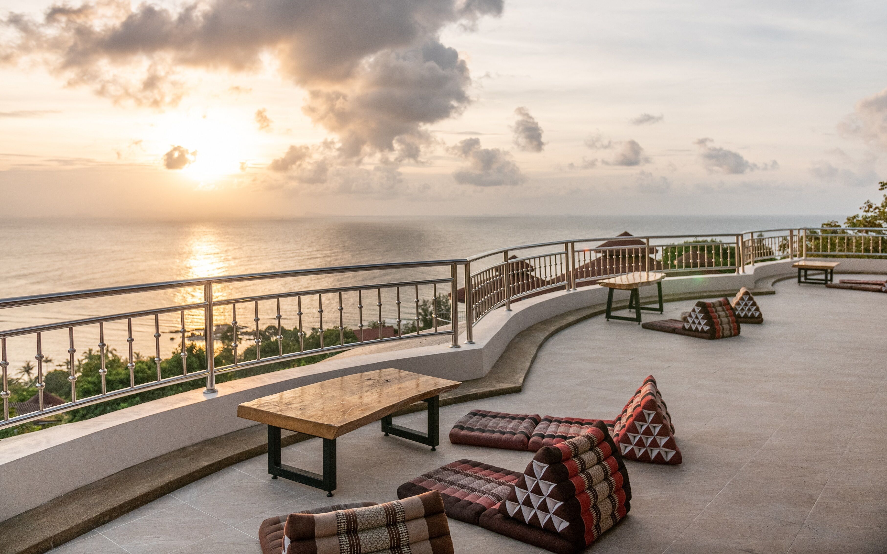 A terrace with a view of the sea, featuring a table, chairs, and a railing.