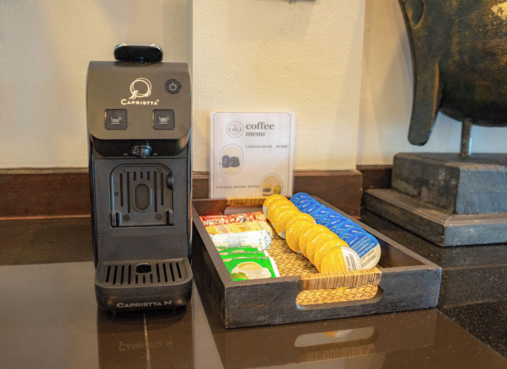 Una cafetera con la etiqueta 'Cafristta' y una bandeja con cápsulas de café y un menú de café.