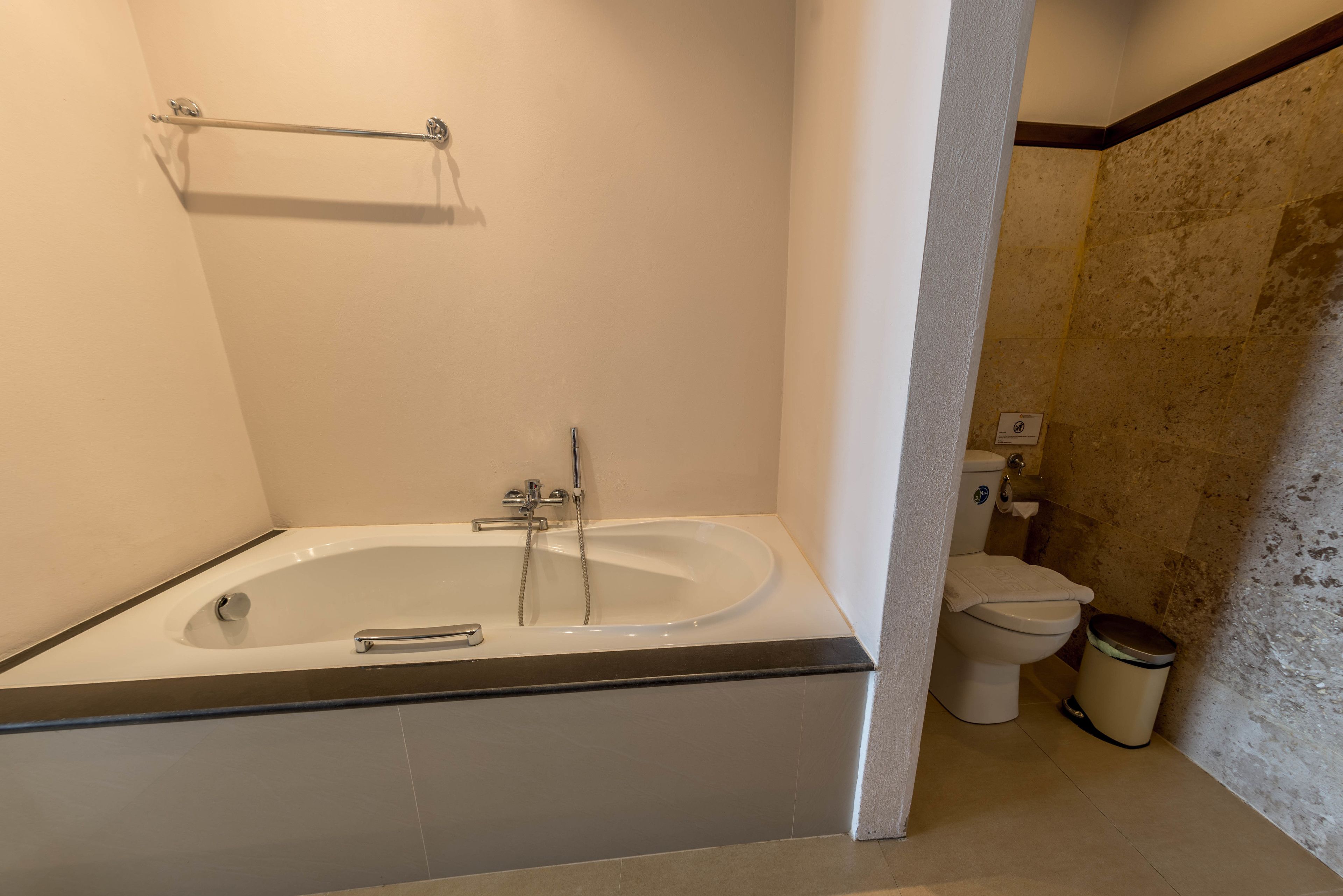 A bathroom with a bathtub, toilet, and trash can.
