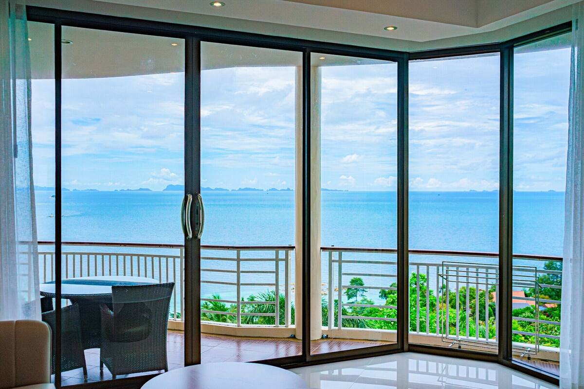 A spacious balcony with large glass doors, offering a view of the sea and distant land.