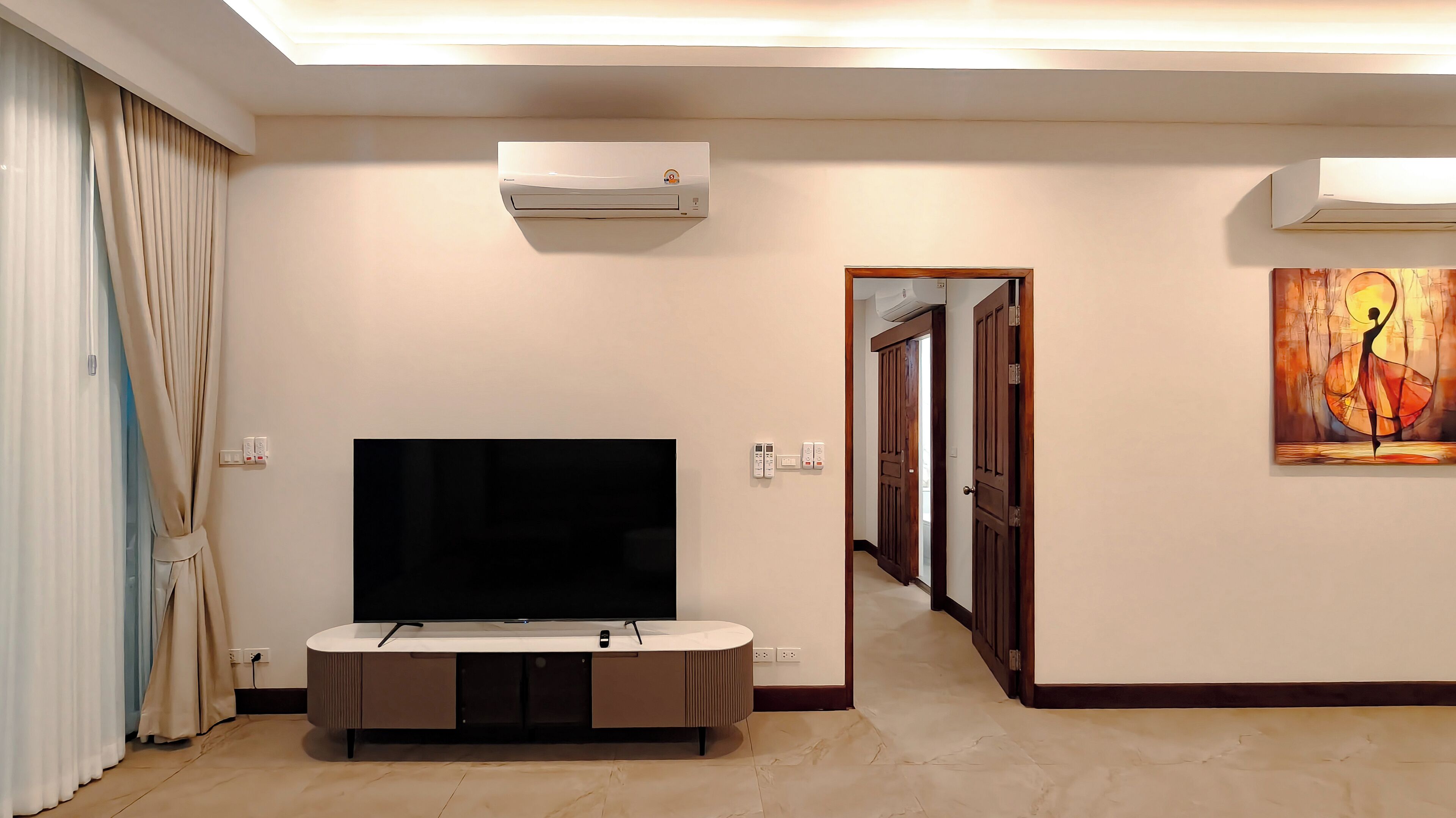A modern living room with a flat-screen TV, built-in air conditioning, and a painting on the wall.