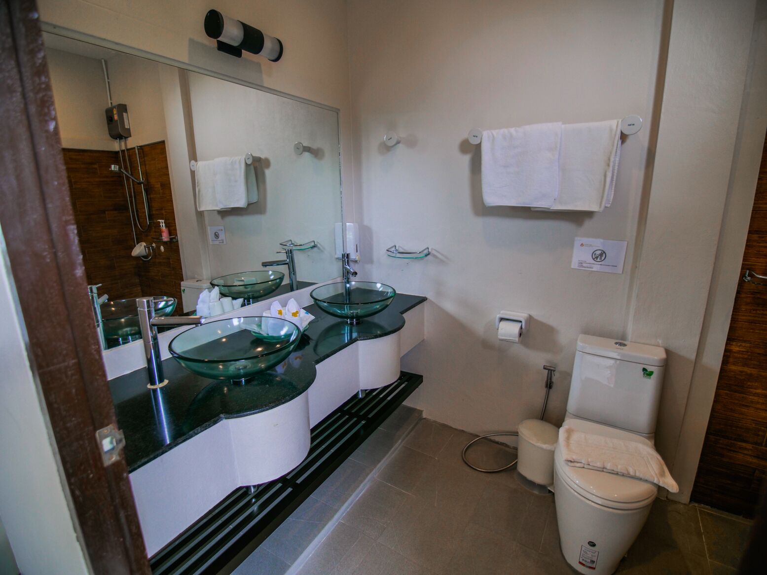 A modern bathroom with two glass sinks, a toilet, and a shower.