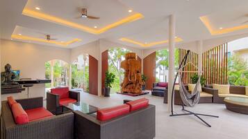 Un espacio interior amplio con mobiliario de mimbre, una gran escultura de madera y vistas al exterior con vegetación.