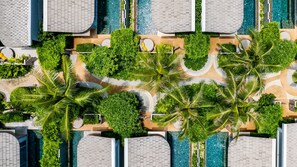 An aerial view of a resort with multiple swimming pools, palm trees, and a tiled walkway.
