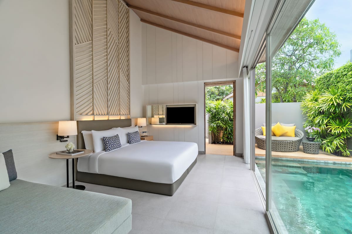 A modern bedroom with a large bed, bedside tables, a TV, and a view of an outdoor swimming pool.