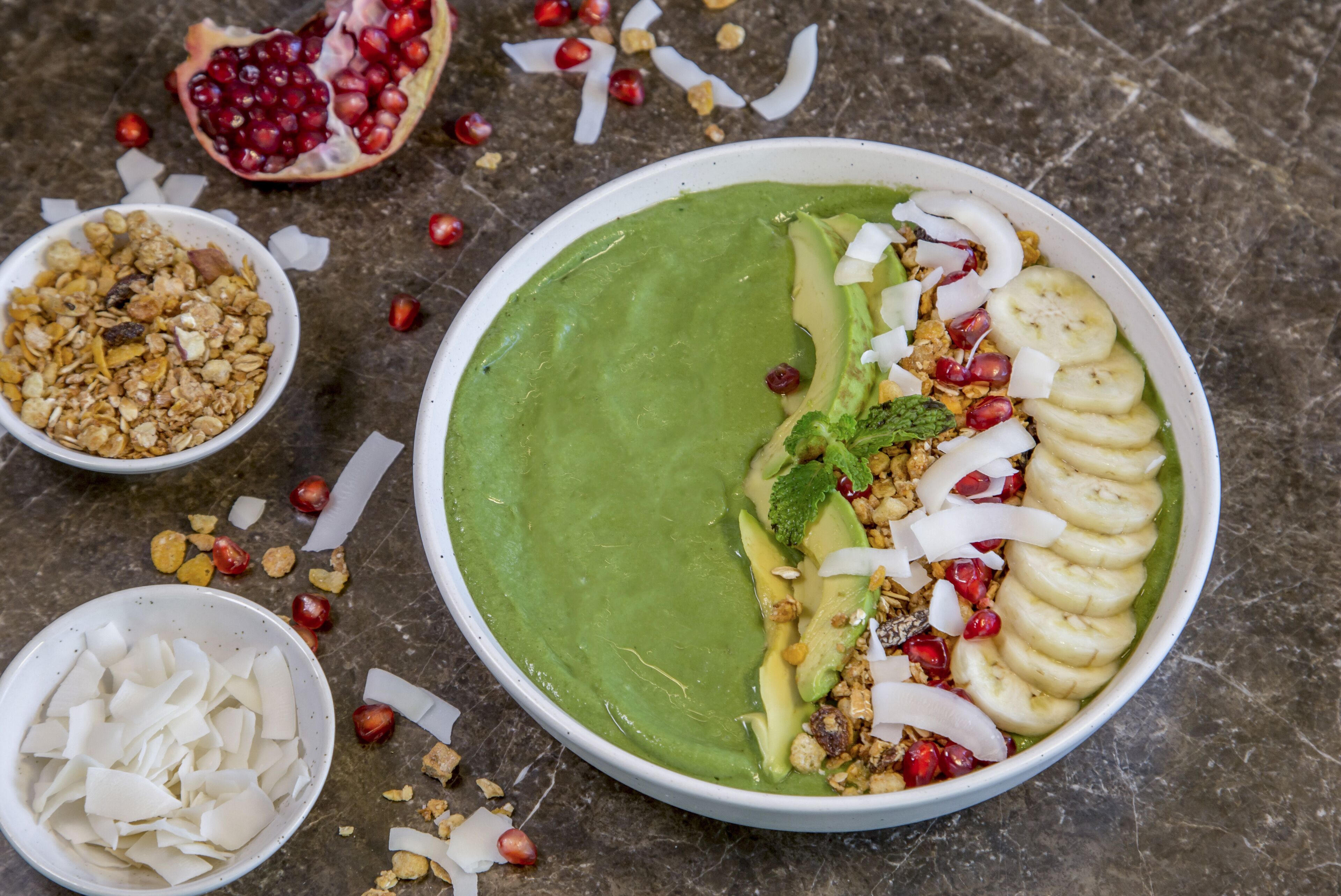 Ein Smoothie aus grünem Gemüse mit Bananenscheiben, Granatapfelkernen und Granola.