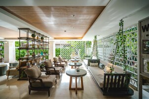Un interior moderno con techo de madera, zona de estar con sofás y sillones, estantería y pared con diseño de celosía y plantas colgantes.