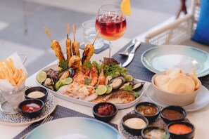 A seafood platter with various grilled items, a glass of red wine, and several small bowls of dipping sauces.