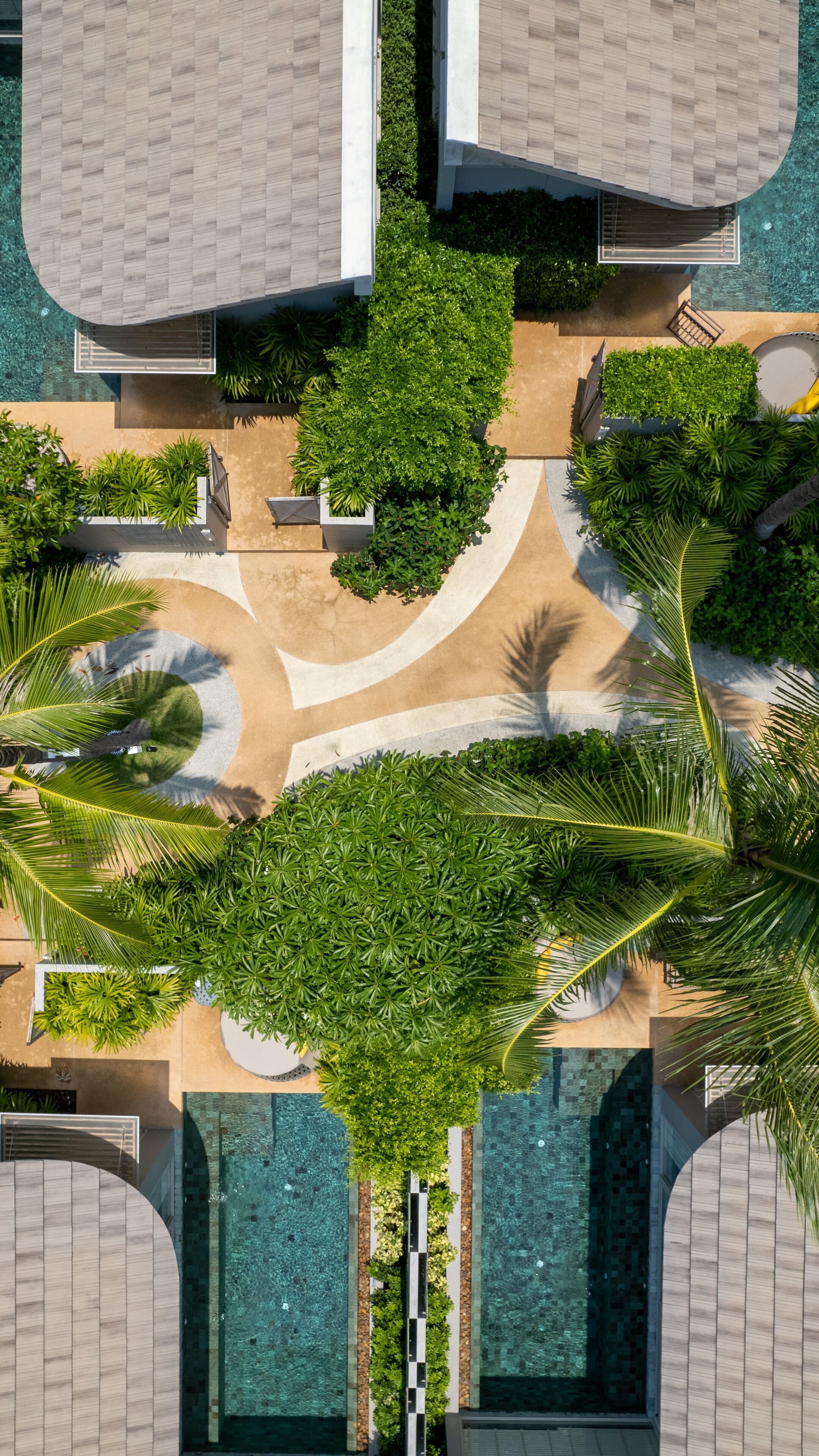 Vista aérea de um resort com várias piscinas, vegetação exuberante e um caminho central.