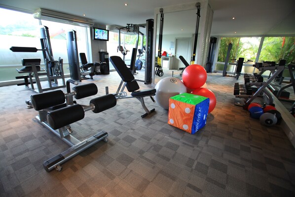 A gym with various exercise equipment, a large window, and a TV screen.